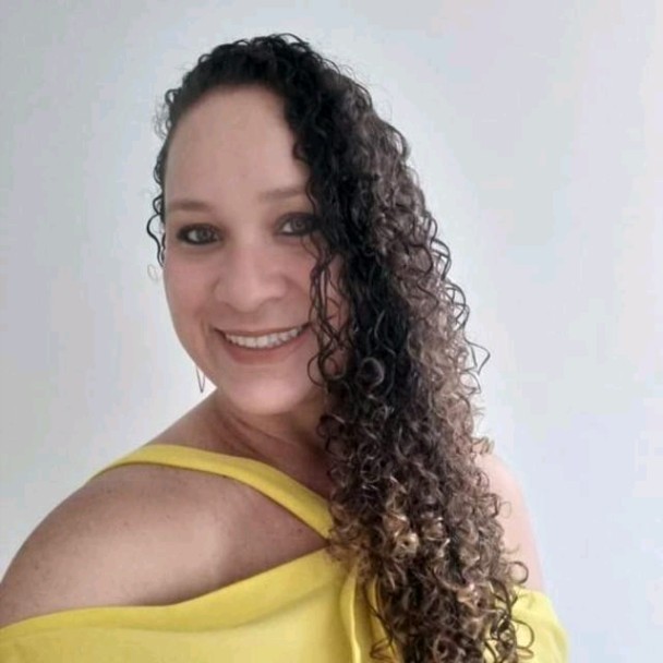 Foto de Evana Carvalho, aluna do curso de Design de Conteúdo Acessível, uma mulher branca sorrindo de cabelos longos encaracolados, usando uma blusinha amarela.