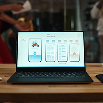 Foto de um notebook em cima de uma mesa com interfaces mobile desenhadas na tela, representando o curso de Interface Visual.
