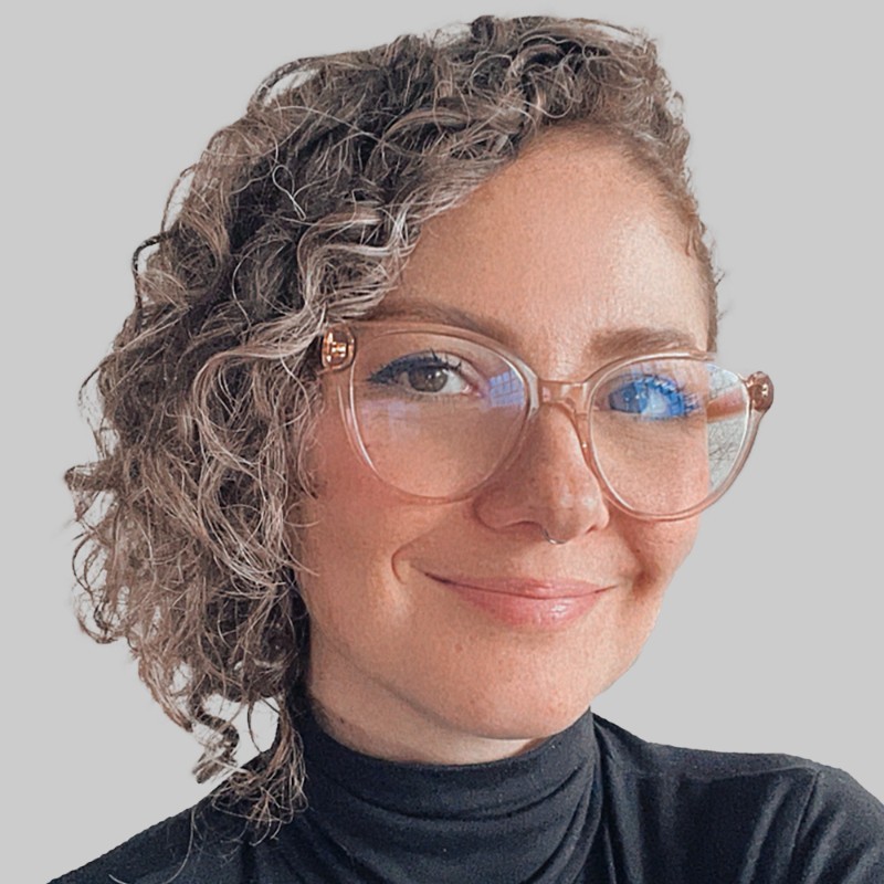 Foto de Linei Marani, palestrante da DEXCONF 2024. Uma mulher branca de cabelo ruivo curto e encaracolado, usando óculos e sorrindo.