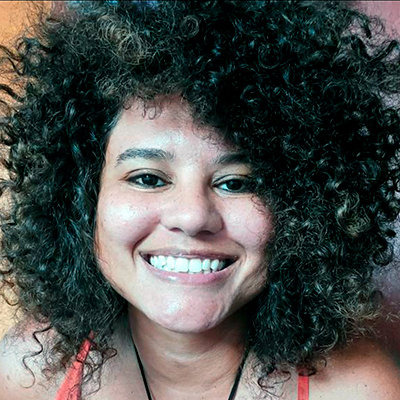 Foto de Samille Souza, palestrante da DEXCONF 2024. Uma mulher negra de pele clara com cabelo crespo estilo black power bem cheio e sorrindo.